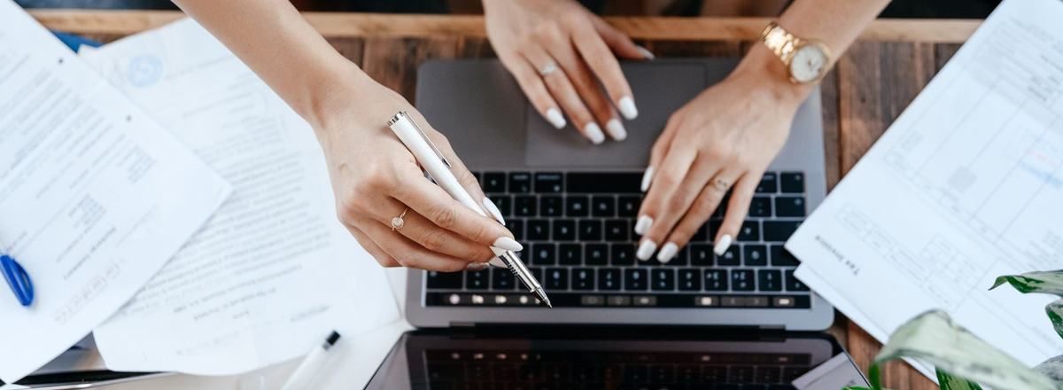 Ręce przy laptopie wśród dokumentów na biurku